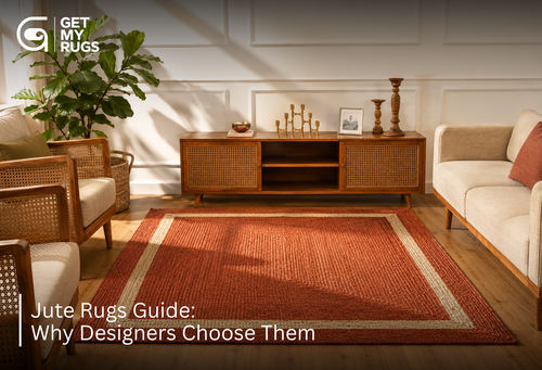Rust-red braided jute area rug with cream border anchoring a sunlit living room with rattan furniture