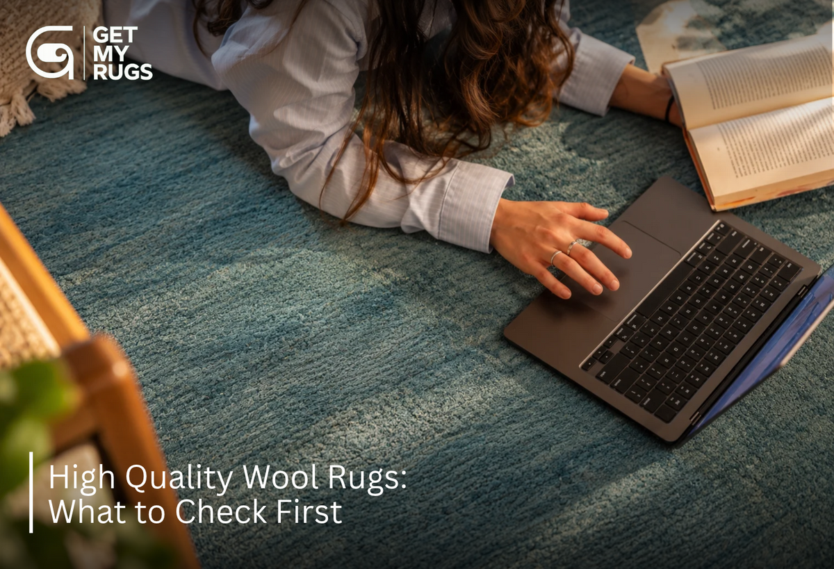 Close-up of a dusty teal wool area rug's heathered texture, with a laptop and book nearby in a lived-in living room